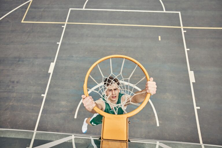 Portrait of basketball player hanging on hoop on a basketball court. Young man playing basketball o